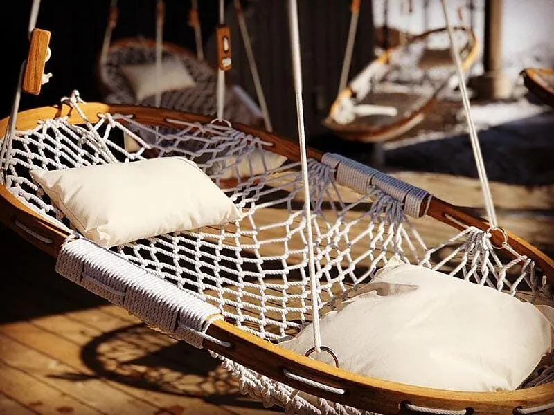 A close up of a Cobble Mountain Hammock Summit Hammock Chair with white pillows. There are two additional Cobble Mountain Summit Hammock Chairs with white pillows in the background.